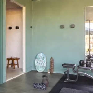 Sfeervolle fitnessruimte met een donkergrijze Hebeta HB betonlook pvc-tegelvloer. De ruimte heeft saliegroene wanden, een trainingsbank met gewichten op een zwarte sportmat, een foamroller, kettlebell en een Indo Board balancetrainer tegen de muur.
