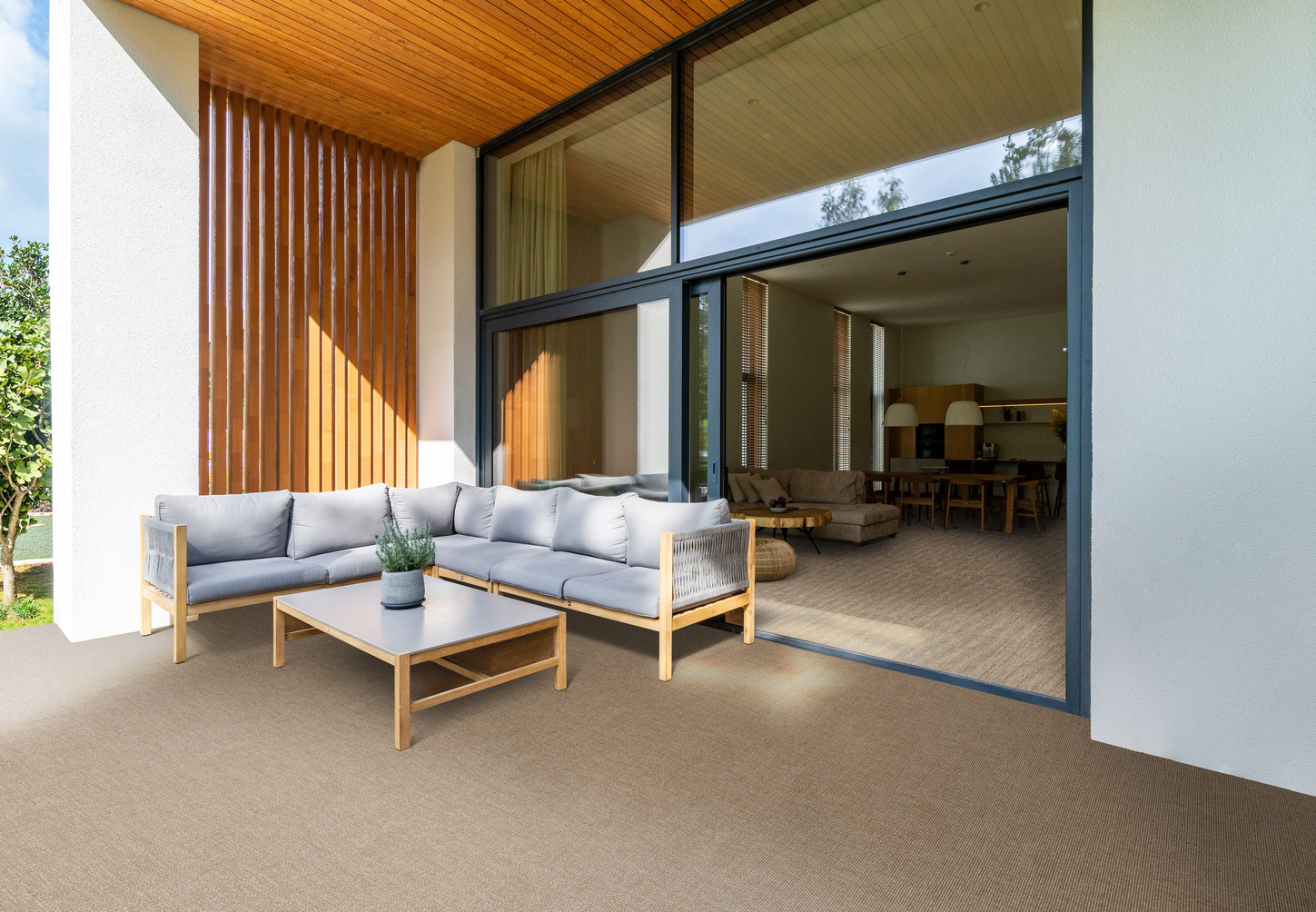 Moderne lichte patio met een grijsbruin, fijn geweven sisal-look tapijt als vloerbedekking, ingericht met een hoekbank en salontafel voor een grote glazen schuifpui.
